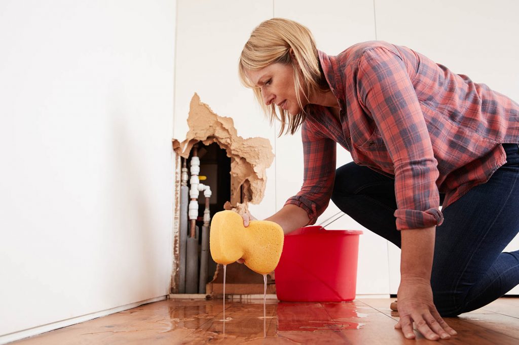 worried woman mopping up water from a burst pipe w P3WL6FN